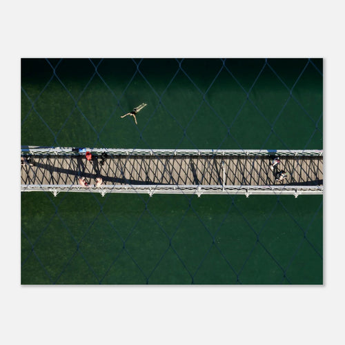 Aerial photo of a swimmer in bright green water beside a footbridge, seen through a fence, summer wall art poster
