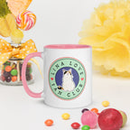 White ceramic mug with pink rim and handle featuring circular Lina Love Fan Club logo with calico cat illustration and heart accents.