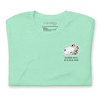 Mint green unisex t-shirt with Be Loving neck label and small Lina Love cat illustration with flowers and the text “The horrors persist, but so do the snacks” printed on the chest.